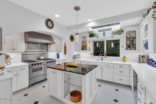 kitchen featuring range with two ovens, wall chimney range hood, decorative backsplash, and a sink