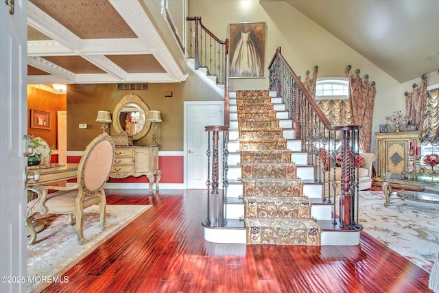 stairs with beam ceiling, hardwood / wood-style floors, a towering ceiling, visible vents, and coffered ceiling