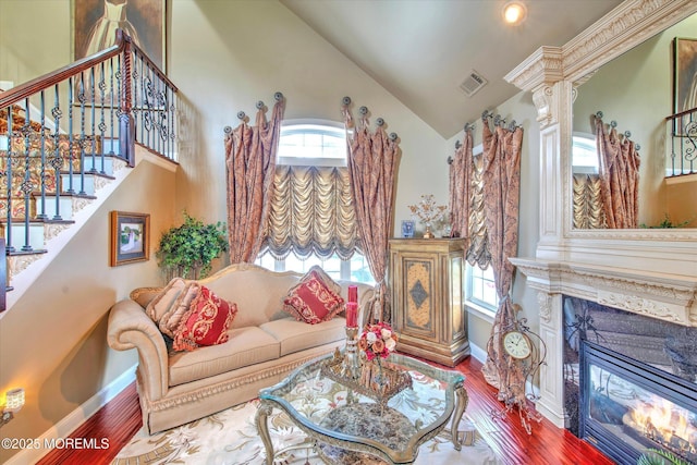 living room featuring a fireplace, high vaulted ceiling, baseboards, wood finished floors, and visible vents