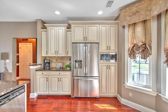 kitchen featuring dark wood finished floors, stainless steel appliances, decorative backsplash, cream cabinetry, and visible vents