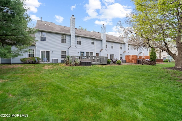 rear view of property featuring a chimney, a wooden deck, cooling unit, and a lawn