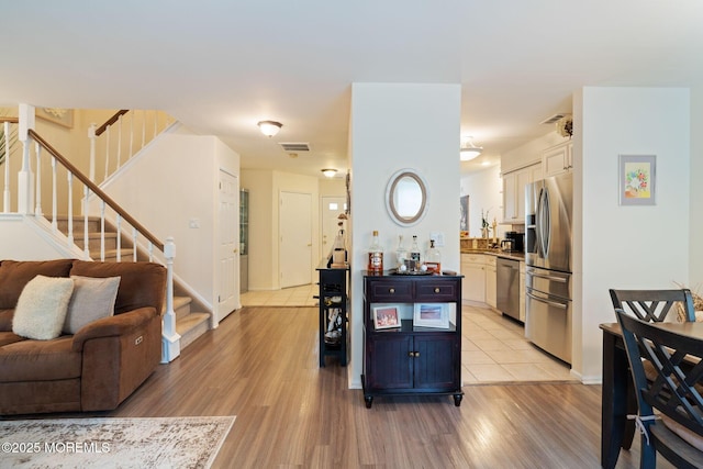 living area with stairs, visible vents, and light wood-type flooring