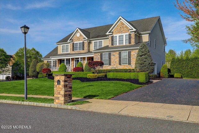 view of front of home with a front yard, covered porch, and stone siding