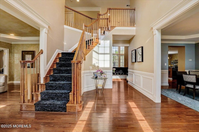 entrance foyer featuring crown molding, wainscoting, wood finished floors, and stairway