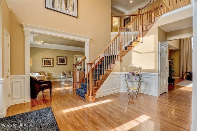 staircase with a wainscoted wall, ornamental molding, a decorative wall, and wood finished floors