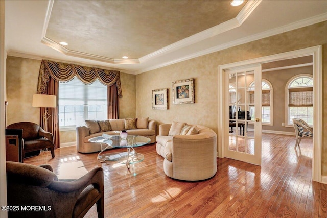 living room with baseboards, ornamental molding, a tray ceiling, and hardwood / wood-style flooring