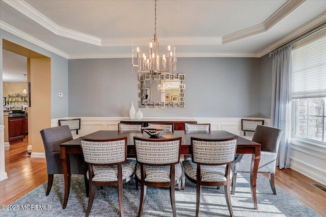 dining space with a chandelier, ornamental molding, wood finished floors, and a raised ceiling