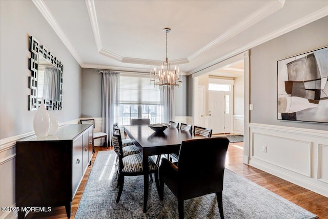 dining space with an inviting chandelier, light wood-style floors, plenty of natural light, and a tray ceiling