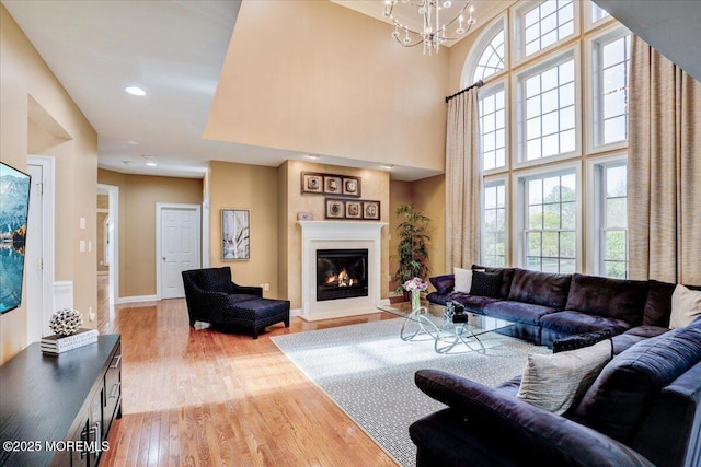 living area with wood finished floors, baseboards, a glass covered fireplace, an inviting chandelier, and recessed lighting
