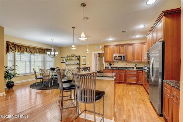kitchen with appliances with stainless steel finishes, light wood finished floors, a kitchen breakfast bar, brown cabinetry, and visible vents