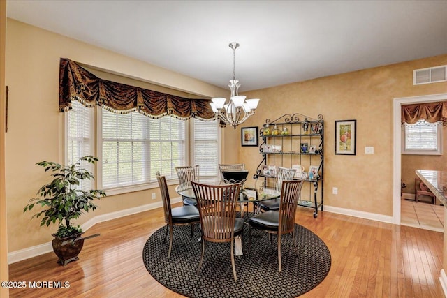 dining space with visible vents, light wood-style floors, baseboards, and a chandelier