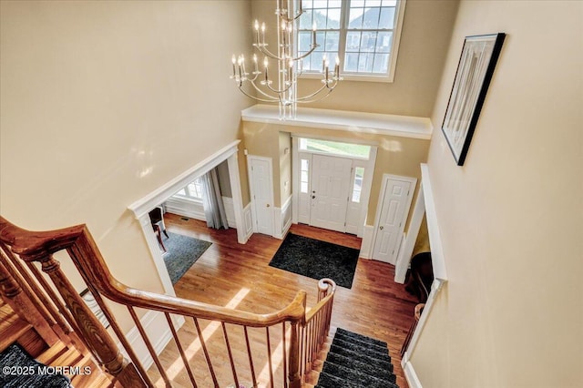 foyer featuring an inviting chandelier, a wealth of natural light, wood finished floors, and a towering ceiling