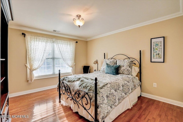 bedroom with crown molding, baseboards, visible vents, and wood finished floors