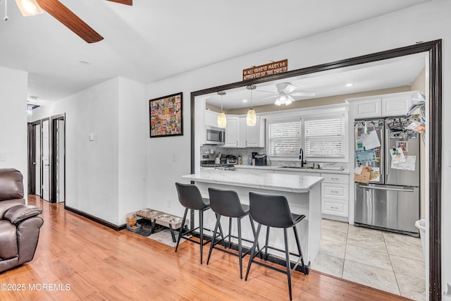 kitchen featuring a breakfast bar area, white cabinets, ceiling fan, and appliances with stainless steel finishes