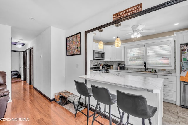 kitchen featuring a kitchen breakfast bar, a sink, white cabinets, and appliances with stainless steel finishes