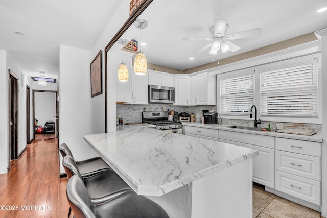 kitchen with appliances with stainless steel finishes, white cabinets, ceiling fan, a sink, and a peninsula
