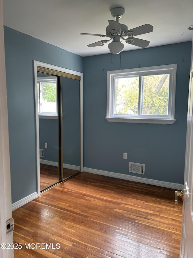 unfurnished bedroom featuring baseboards, visible vents, hardwood / wood-style flooring, and a closet