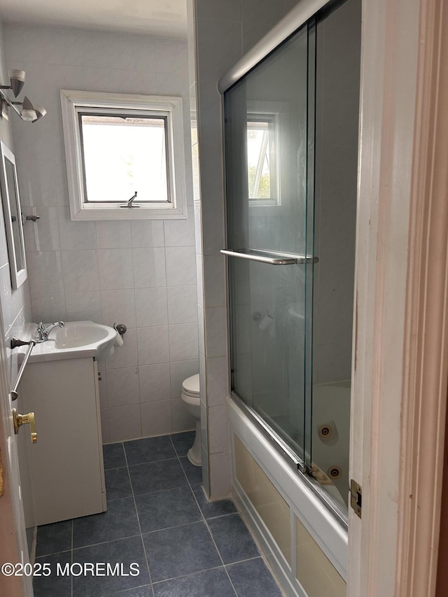 full bath with tile patterned flooring, combined bath / shower with glass door, tile walls, toilet, and vanity