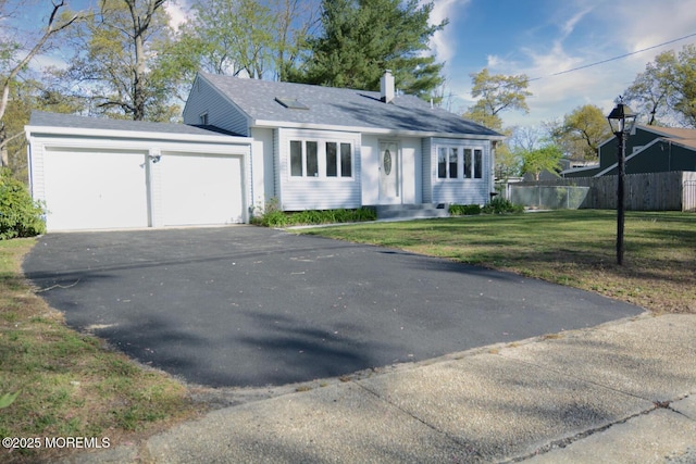 view of front facade with a front yard, driveway, a chimney, an attached garage, and fence