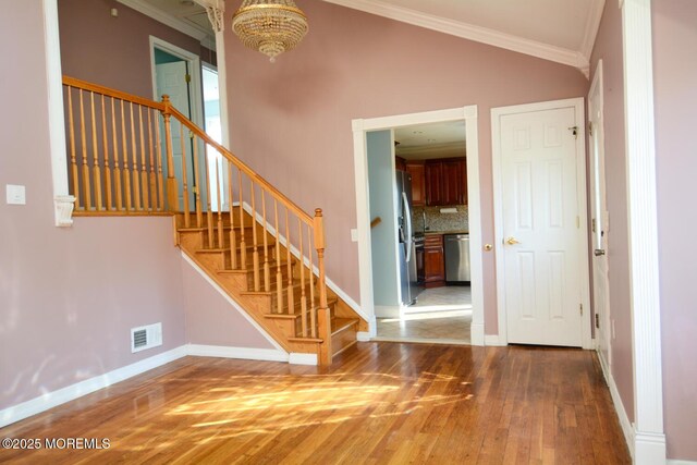 entryway with wood finished floors, stairs, ornamental molding, visible vents, and a notable chandelier