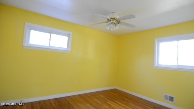 unfurnished room with a ceiling fan, visible vents, wood finished floors, and baseboards
