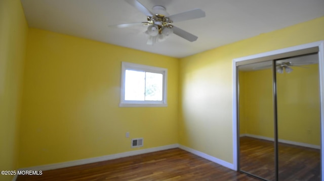 unfurnished bedroom featuring a closet, visible vents, baseboards, and dark wood finished floors