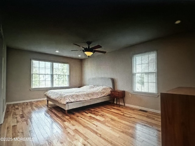 bedroom with wood finished floors, baseboards, and multiple windows