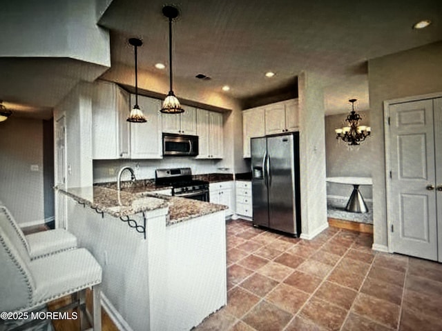 kitchen with dark stone counters, white cabinets, stainless steel appliances, a peninsula, and hanging light fixtures