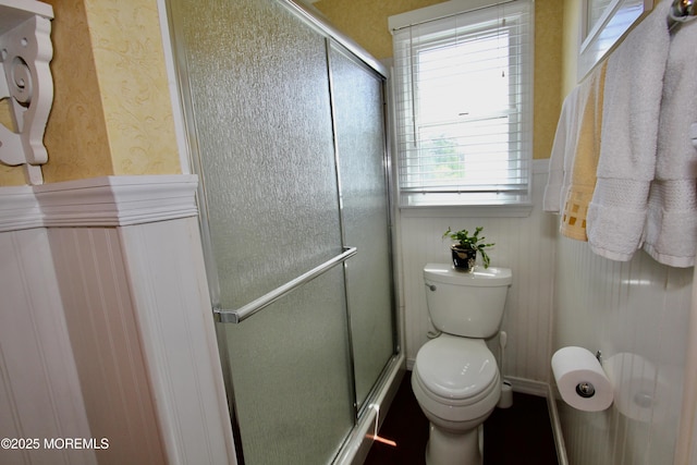 bathroom with toilet, a stall shower, and wainscoting