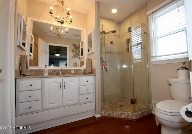 bathroom with wood finished floors, a shower stall, ceiling fan with notable chandelier, toilet, and vanity