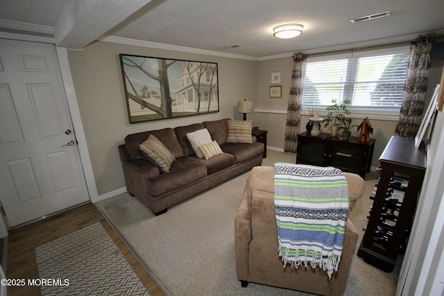 living area with baseboards, visible vents, ornamental molding, and wood finished floors