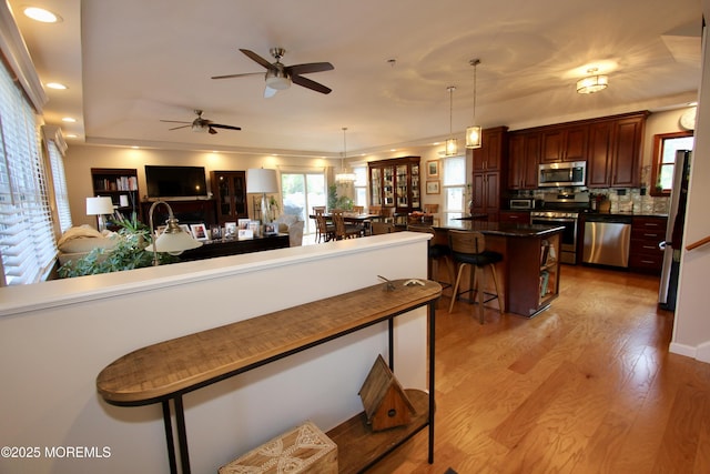 kitchen with a breakfast bar area, light wood-style floors, appliances with stainless steel finishes, dark countertops, and backsplash