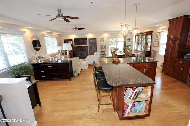 kitchen featuring a breakfast bar area, light wood-style flooring, ceiling fan, a glass covered fireplace, and a large island