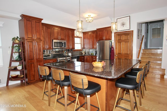 kitchen with a breakfast bar, appliances with stainless steel finishes, light wood-style flooring, and decorative backsplash