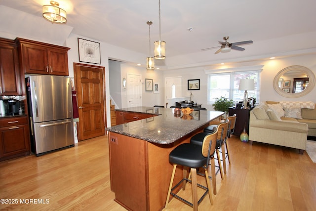 kitchen featuring a breakfast bar area, freestanding refrigerator, open floor plan, light wood finished floors, and a ceiling fan