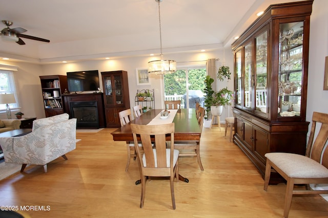 dining space with a wealth of natural light, a tray ceiling, light wood-style floors, and a glass covered fireplace