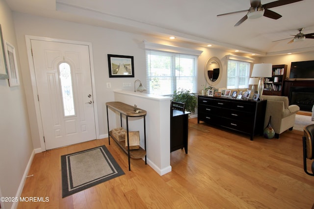 foyer entrance featuring a fireplace, ceiling fan, baseboards, and light wood-style floors