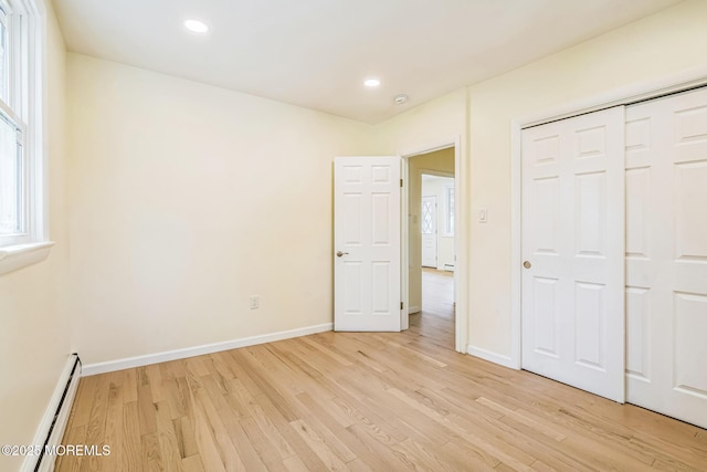 unfurnished bedroom featuring baseboards, a baseboard heating unit, and light wood-style floors