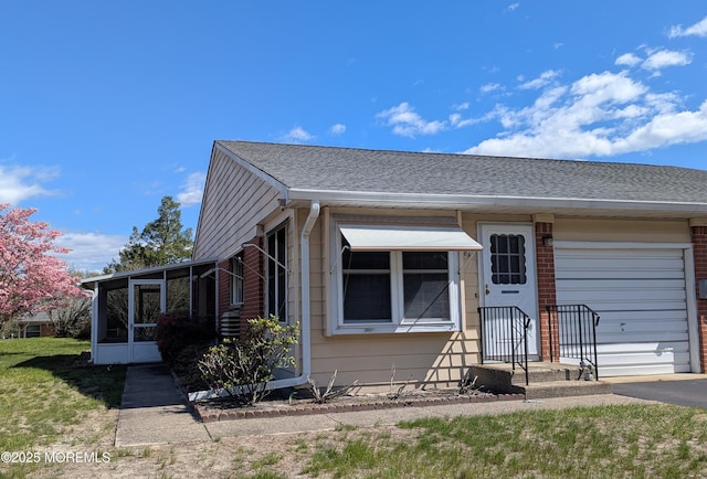 view of front of property featuring driveway, a garage, a shingled roof, and a sunroom