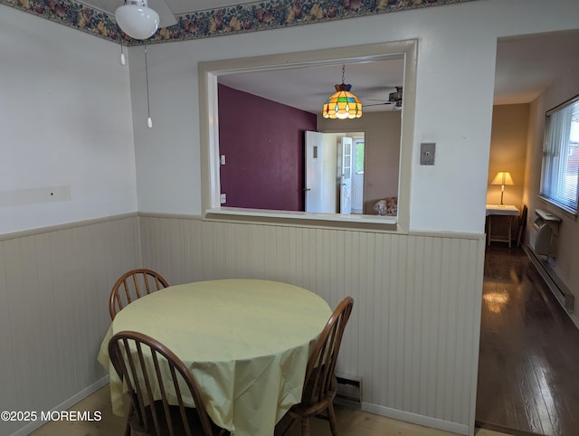 dining space with a wainscoted wall, a ceiling fan, wood finished floors, and a baseboard radiator