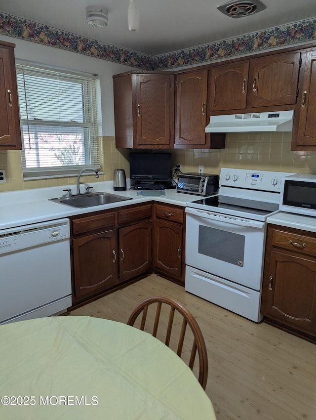 kitchen featuring white appliances, light wood-style flooring, decorative backsplash, under cabinet range hood, and a sink
