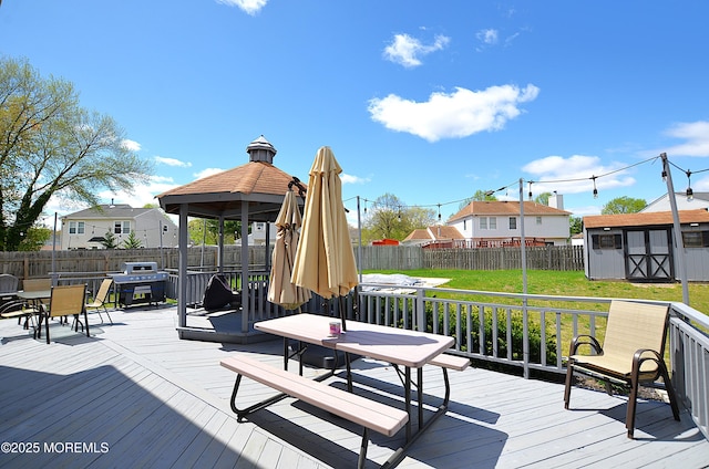 deck featuring outdoor dining area, an outbuilding, a gazebo, a fenced backyard, and a shed