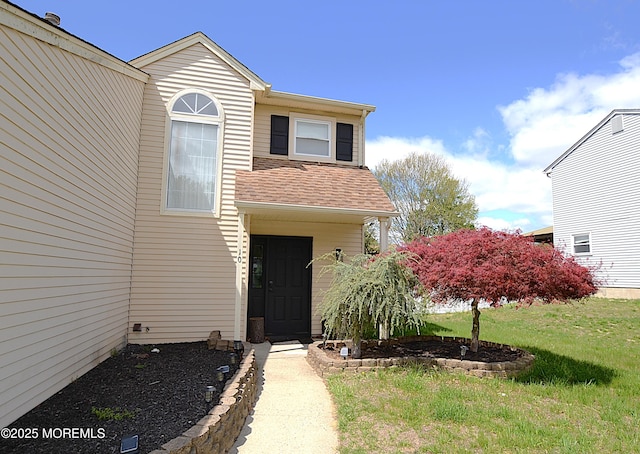 view of exterior entry featuring a lawn and a shingled roof