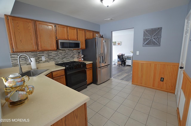 kitchen featuring appliances with stainless steel finishes, a sink, light countertops, a wainscoted wall, and visible vents