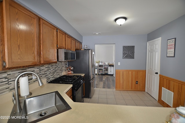kitchen featuring a sink, brown cabinetry, a wainscoted wall, stainless steel appliances, and visible vents