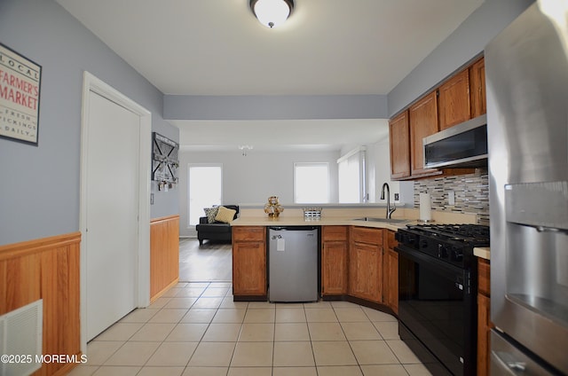 kitchen with brown cabinetry, appliances with stainless steel finishes, a sink, light countertops, and a peninsula