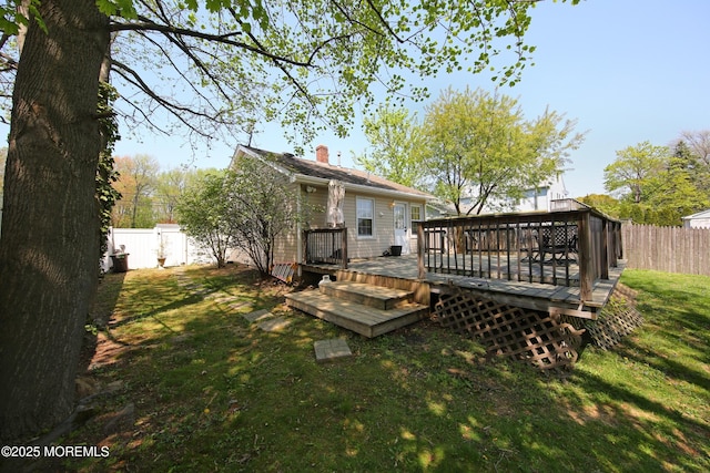 rear view of property featuring a chimney, a fenced backyard, a deck, and a yard