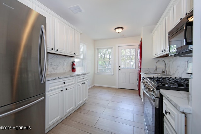 kitchen featuring tasteful backsplash, white cabinets, a sink, visible vents, and stainless steel appliances
