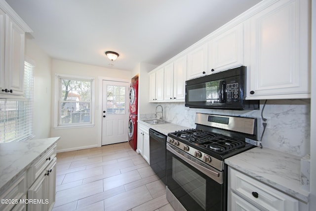 kitchen with stacked washer / drying machine, a sink, tasteful backsplash, black appliances, and white cabinets
