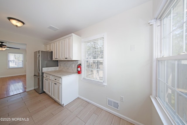 kitchen with decorative backsplash, visible vents, freestanding refrigerator, baseboards, and light wood-type flooring